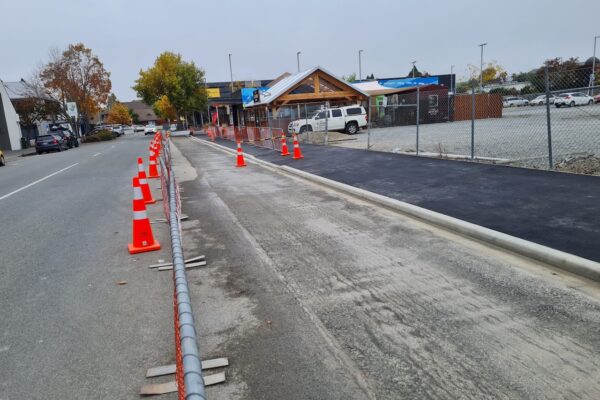 Roading crew completing kerb, channel and footpath upgrades with traffic cones and fencing guiding vehicles and pedestrians through the work zone.