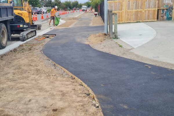 Freshly laid asphalt pathway being shaped and finished as part of subdivision footpath construction, with compacting and trimming works underway.