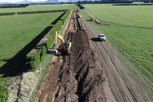 Aerial view of excavators trenching across rural farmland to install a long-run trunk main, with service vehicles accessing the alignment.