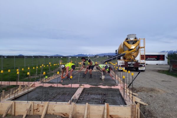 Construction crew placing and levelling concrete over reinforcing steel for a new foundation slab at a rural Canterbury worksite.