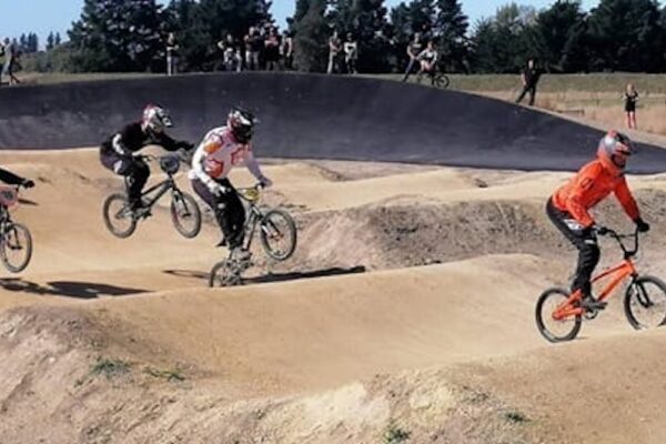 BMX riders competing on a newly formed pump track with shaped dirt features, demonstrating the completed earthworks and track development.