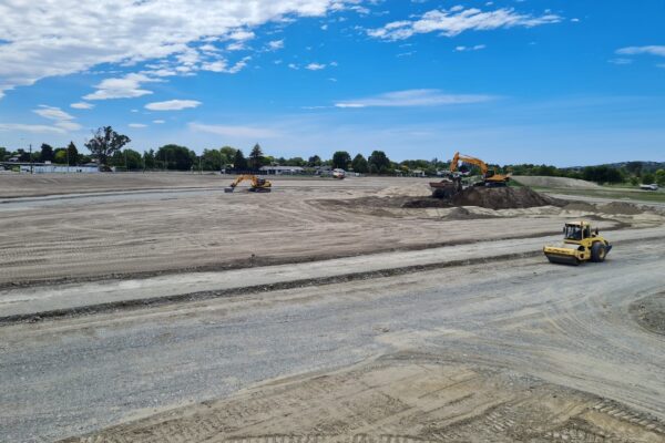 Large-scale earthworks for a new subdivision with excavators, rollers and trucks shaping the site for future roads, sections and drainage systems.