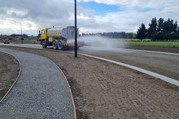Water cart spraying a new roadway under construction, with machinery working across the subdivision and newly formed footpaths in the foreground.