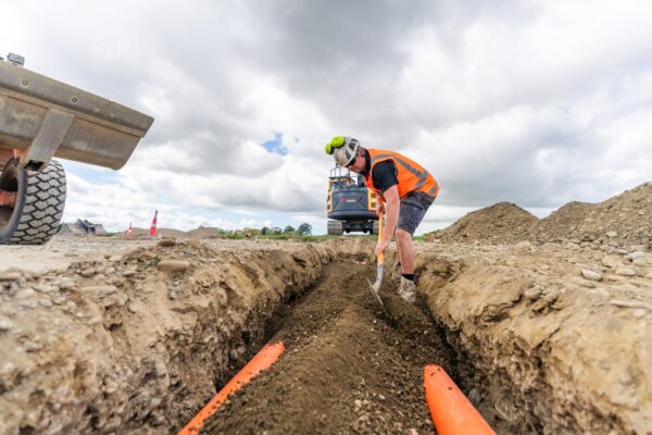 Workers assemble fittings for water reticulation within the trench, forming an essential part of the civil drainage system for the development.