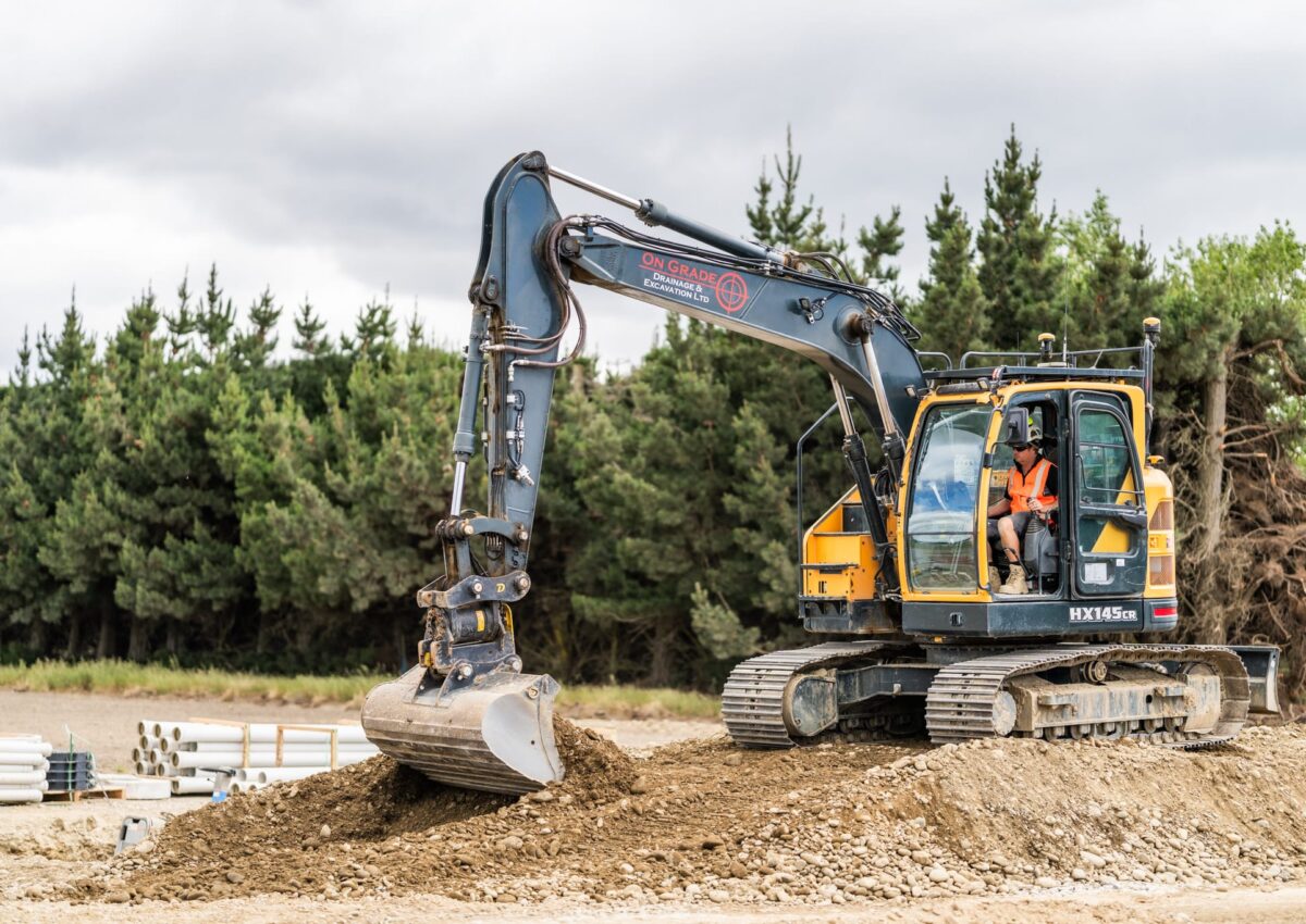 A compact excavator shapes material with precision, supporting efficient site works as the drainage and earthmoving tasks progress.