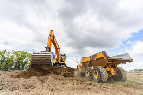 The excavator loads the dump truck, the two machines working in sync to clear and cart material efficiently.