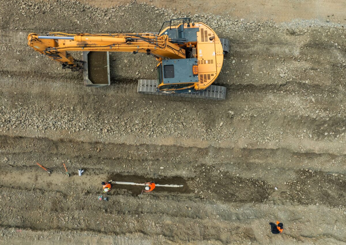 Overhead image of an excavator and civil construction crew carrying out land excavation and deep drainage for storm water solutions, wastewater treatment connections and water reticulation systems on a large civil engineering Christchurch project.