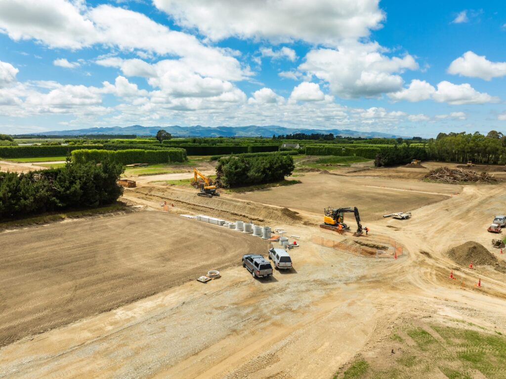 A wide view of subdivision earthworks with excavations, civil construction machinery and civil contractors preparing land for stormwater drainage, water reticulation and wastewater treatment systems as part of large construction projects managed by a civil engineering company and construction contractor in Canterbury.