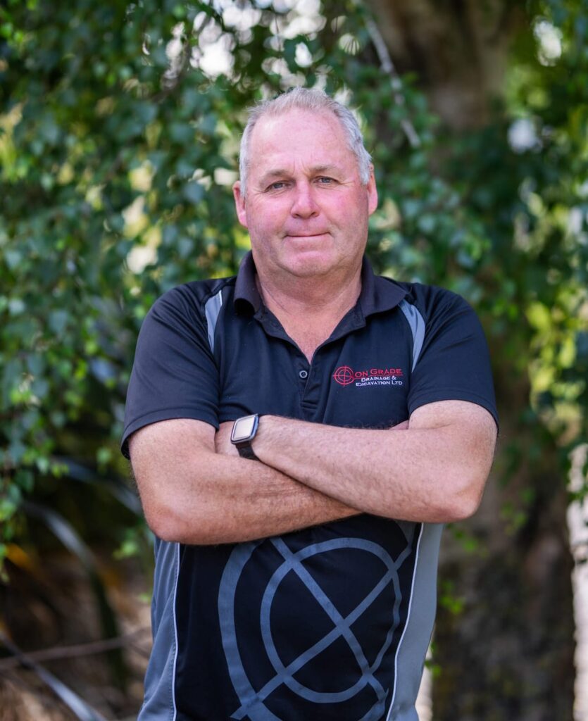 Experienced civil contractor outdoors in branded uniform, representing earthworks company services including storm water drainage systems, water reticulation systems, wastewater reticulation system work, kerb and channel, footpaths and wider civil construction projects.