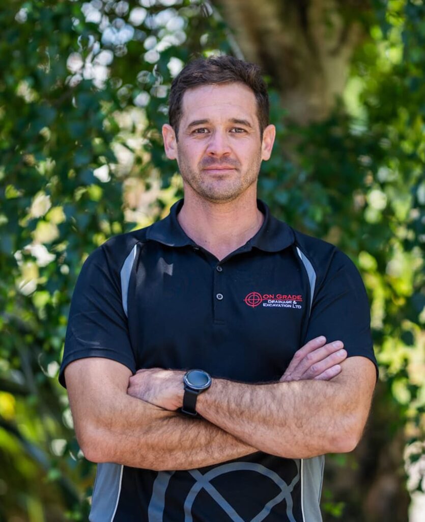 Team member in high-vis uniform standing outdoors, highlighting stormwater systems, storm water tank installation, earthworks company expertise, wastewater treatment, water reticulation and civil construction services for subdivisions.